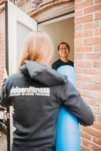 man greets woman holding exercise roller at door