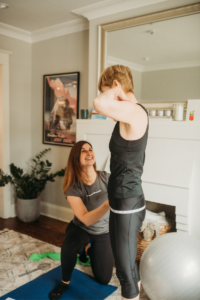 woman in black smiling while trainer measures hip circumference