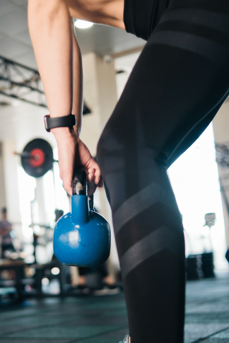 woman in black leggings lifts blue kettlebell
