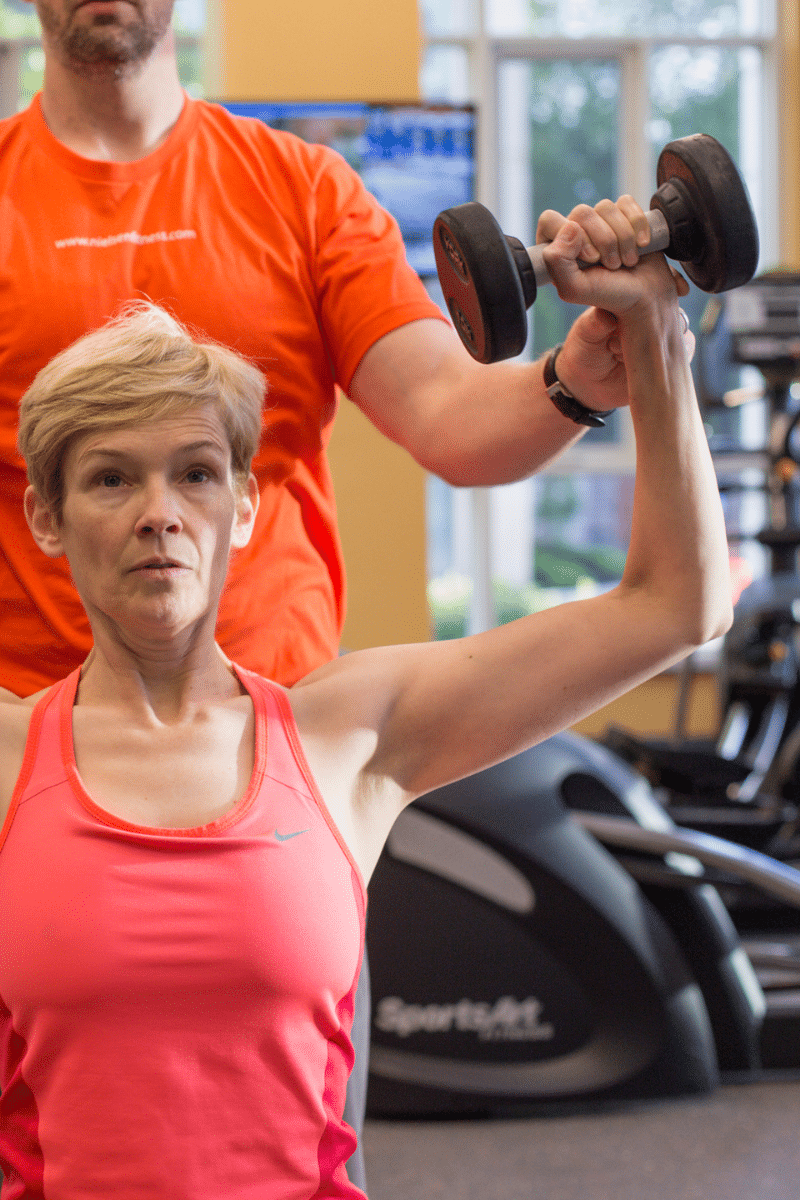 a personal trainer assists a client with an overhead press